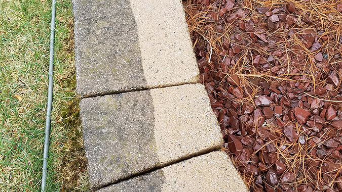 Half of a retaining wall pressure washed to show before and after